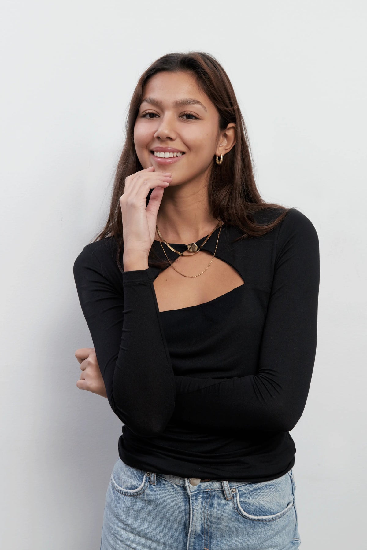 Close up on a model smiling and wearing an elegant long sleeves black top with a triangle cut-out and a golden button closure. The top is made with Tencel™Modal fabric.